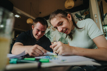 A young man with Down syndrome and a girl in a wheelchair sharing a joyful moment as they draw and...
