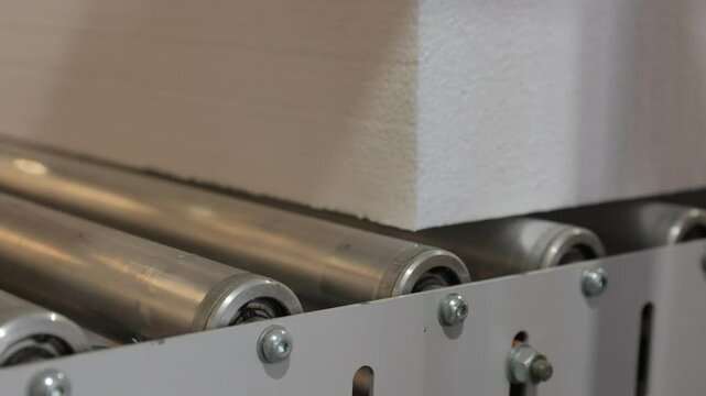Close-up of a large foam block moving smoothly on a conveyor belt in a factory. The shot highlights industrial automation and precision in modern manufacturing processes.
