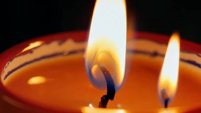 A candle is lit and the flame is yellow. The candle is in a red bowl