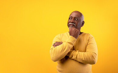 Thoughtful senior African American man looking aside at empty space, touching his chin, deep in...