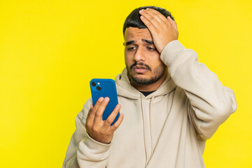 Upset sad Indian young man use smartphone typing browsing, play game, loses, surprised by sudden...