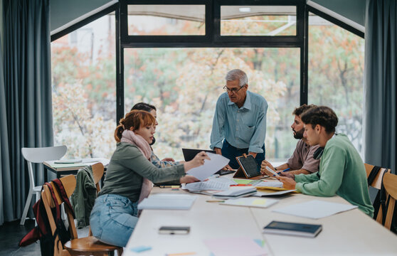 A group of university students working together on a project, receiving guidance from a senior professor in a classroom setting.