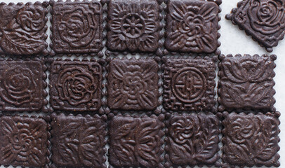 Overhead view of stamped dark molasses cookies on a parchment lined baking tray, top view of embossed gingerbread cookies on a white background