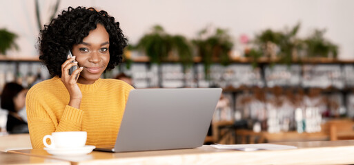 Black lady entrepreneur working with laptop at cafe, having business conversation on mobile phone