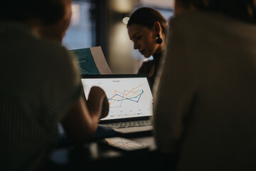A diverse group of business professionals engages in analyzing financial data on a laptop in an urban office, highlighting global collaboration and teamwork.