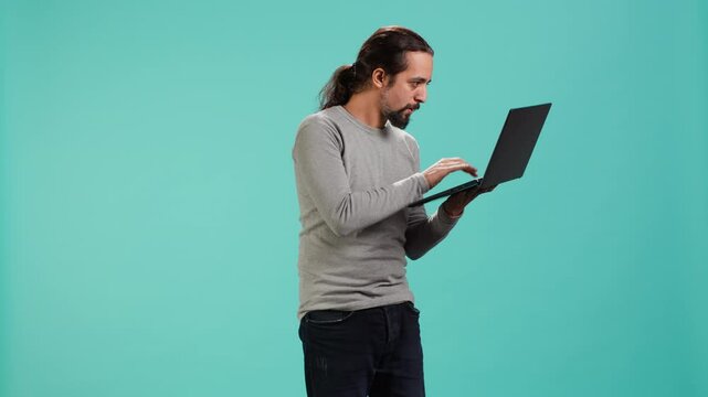 Upset man frowns while looking at laptop, dissatisfied with company profits, studio backdrop. Irked worker flabbergasted by low business income revenue, doing financial analysis on notebook, camera A