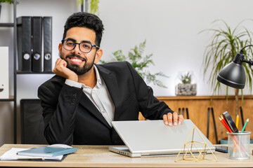 Portrait of Indian bearded businessman face freelancer at home office modern workplace working on laptop computer. Manager freelancer Arabian man works on notebook send messages makes online purchases