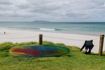 Surfboard leaning up against a fencepost and wet suit drying on a calm sunny day at Te Arai Beach,...