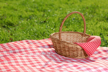 One picnic wicker basket with checkered napkin and blanket on green grass. Space for text