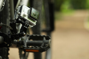 Modern action camera with mount on bicycle outdoors, closeup. Space for text