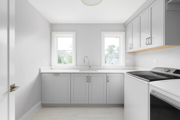 A laundry room with grey cabinets, white marble countertop, white washer and dryer, and a brown...