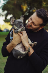 man hugging a dog, walk in the park, outside french bulldog puppy with owner, man with pet spending time outside the house, happy smiling people with a dog