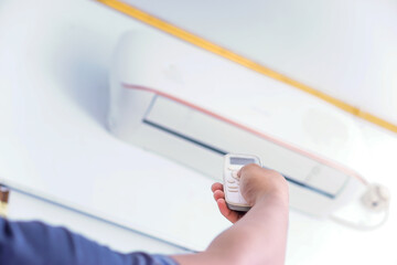 A person using a remote control to adjust an air conditioning unit mounted on the wall.