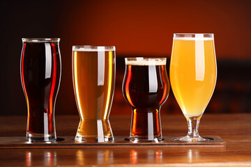Glasses with different types of beer on wooden table against color background