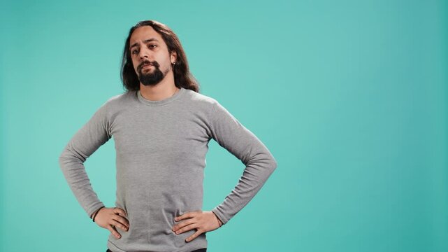 Portrait of man standing confidently with hands on hips, posing against plain studio background, projecting confidence and strength. Person holding assertive stance posture, camera B