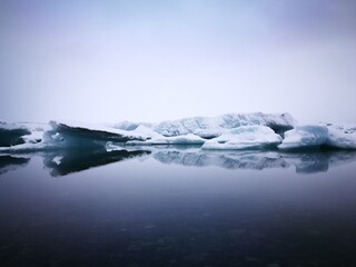 Fototapeta premium A breathtaking winter landscape featuring an iceberg floating in the icy sea, surrounded by snow-covered mountains and a serene lagoon under a clear blue sky
