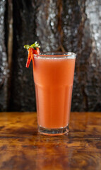 Vaso de jugo natural de frutilla con decoración de frutilla y hojas de menta, sobre mesa de madera rústica. Fondo cálido y natural