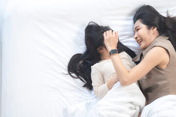 A joyful mother and daughter laughing together while lying on a bed. The playful moment showcases their strong bond and happiness in a comfortable home setting, surrounded by natural decor.