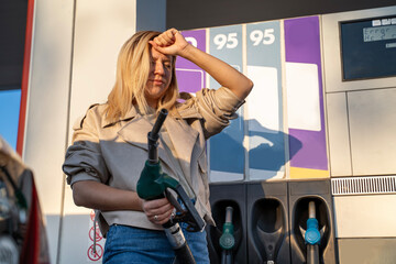 Young woman puts wrong fuel into her car, or expansive gas concept. Woman regretting holding fuel...