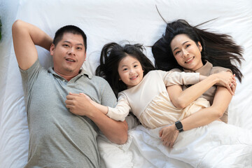 Obraz premium A joyful mother and daughter laughing together while lying on a bed. The playful moment showcases their strong bond and happiness in a comfortable home setting, surrounded by natural decor.