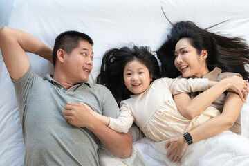 A joyful mother and daughter laughing together while lying on a bed. The playful moment showcases their strong bond and happiness in a comfortable home setting, surrounded by natural decor.