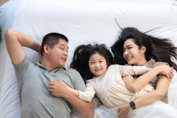 Obraz premium A joyful mother and daughter laughing together while lying on a bed. The playful moment showcases their strong bond and happiness in a comfortable home setting, surrounded by natural decor.