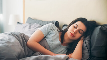 Peaceful morning. Sleeping woman. Lazy weekend. Calm female under blanket closing eyes laying in soft bed sheets light room interior.