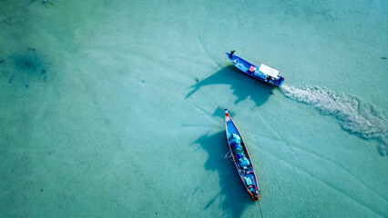 Aerial view of boats floating over turquoise waters in with scattered debris near the shoreline as boat pollutes in sandy waters marine pollution concept