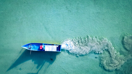 Aerial view of boats floating over turquoise waters in with scattered debris near the shoreline as boat pollutes in sandy waters marine pollution concept