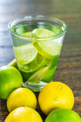 Organic cold refreshing lemonade drink or cocktail made of sparkling water, lime slices and fresh green mint leaves served in tall drinking glass with ice cubes on white wooden table with copy space
