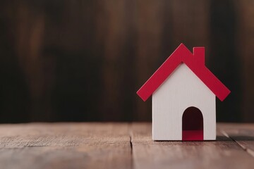 Miniature wooden house model with a red roof on a wooden surface.