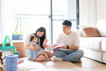 A 1 year old Taiwanese girl spending time playing happily with her parents, a man and woman in their 20s, in a room of a high rise apartment in Taichung City, Taiwan.