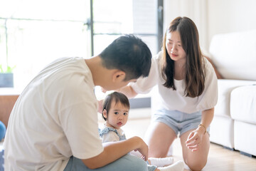 Obraz premium A 1 year old Taiwanese girl spending time playing happily with her parents, a man and woman in their 20s, in a room of a high rise apartment in Taichung City, Taiwan.