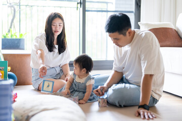 A 1 year old Taiwanese girl spending time playing happily with her parents, a man and woman in their 20s, in a room of a high rise apartment in Taichung City, Taiwan.