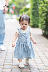 A 1 year old Taiwanese girl walking hand in hand with her parents, a man and woman in their 20s, on a hot sunny day in the streets of Taichung City, Taiwan, in September.