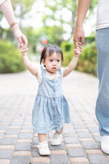 A 1 year old Taiwanese girl walking hand in hand with her parents, a man and woman in their 20s, on a hot sunny day in the streets of Taichung City, Taiwan, in September.