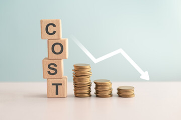 For reduction concept which effect to product cost , profit , inflation and economy recession concept, COST text on wooden cube blocks, stack of coins and decreasing graph