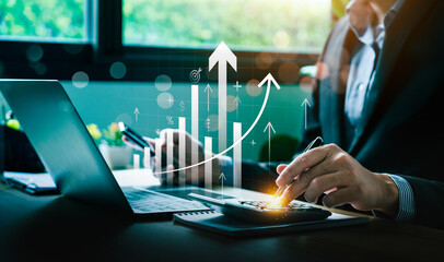 Business Professional Using Calculator and Laptop to Analyze Financial Growth with Rising Bar Graph...