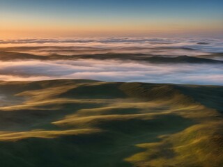 A tranquil dawn sky with wisps of clouds floating close to the ground, bathed in soft morning light as the day begins
