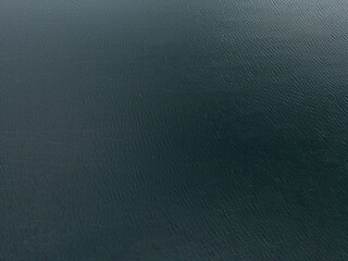 An abstract aerial view of dark, deep water with subtle ripples and mysterious shadows, creating a moody and captivating scene perfect for backgrounds or atmospheric visual