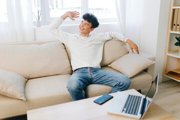 Young man relaxing in a cozy living room, smiling with a casual pose on a sofa, featuring natural light and a stylish interior design