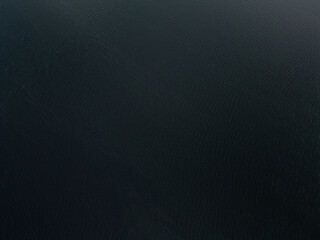 An abstract aerial view of dark, deep water with subtle ripples and mysterious shadows, creating a...