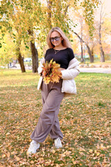 Smiling girl hiding behind autumn leaf in sunny park. Autumn walk playing in autumn park. Vertical image.