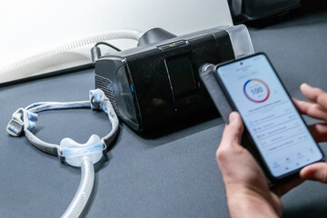 Male European with cpap machine checking therapy analysis via smartphone app or medical app for e-health check and health report via mobile device for health analysis innovative sleep apnea mask apps