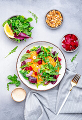 Vegan salad with baked beets, tangerine, red onion, lettuce, sesame and arugula, gray background, top view