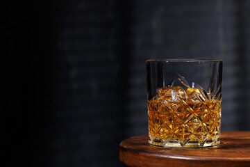A whiskey glass resting on a wooden table, set against a dark background