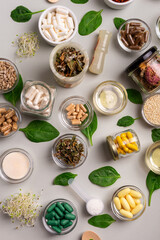 Many homeopathic meds, pills, tablets, herbs, green leaves and other natural organic products in a beautiful composition on a light grey background, top view. Homeopathy and alternative medicine.