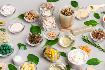 Many homeopathic meds, pills, tablets, herbs, green leaves and other natural organic products in a beautiful composition on a light grey background, top view. Homeopathy and alternative medicine.