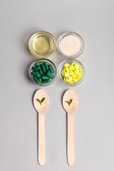Homeopathic medicine. Homeopathic pills in a glass bowls, green leaves on wooden spoons from above on a light grey background. Alternative medicines top view.