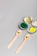 Homeopathic medicine. Homeopathic pills in a glass bowls, green leaves on wooden spoons from above on a light grey background. Alternative medicines top view.